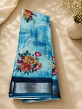 Elegant sky blue floral printed saree featuring a refreshing blend of artistic blue textures and vibrant rose motifs. silver zari border- Cotton Saree