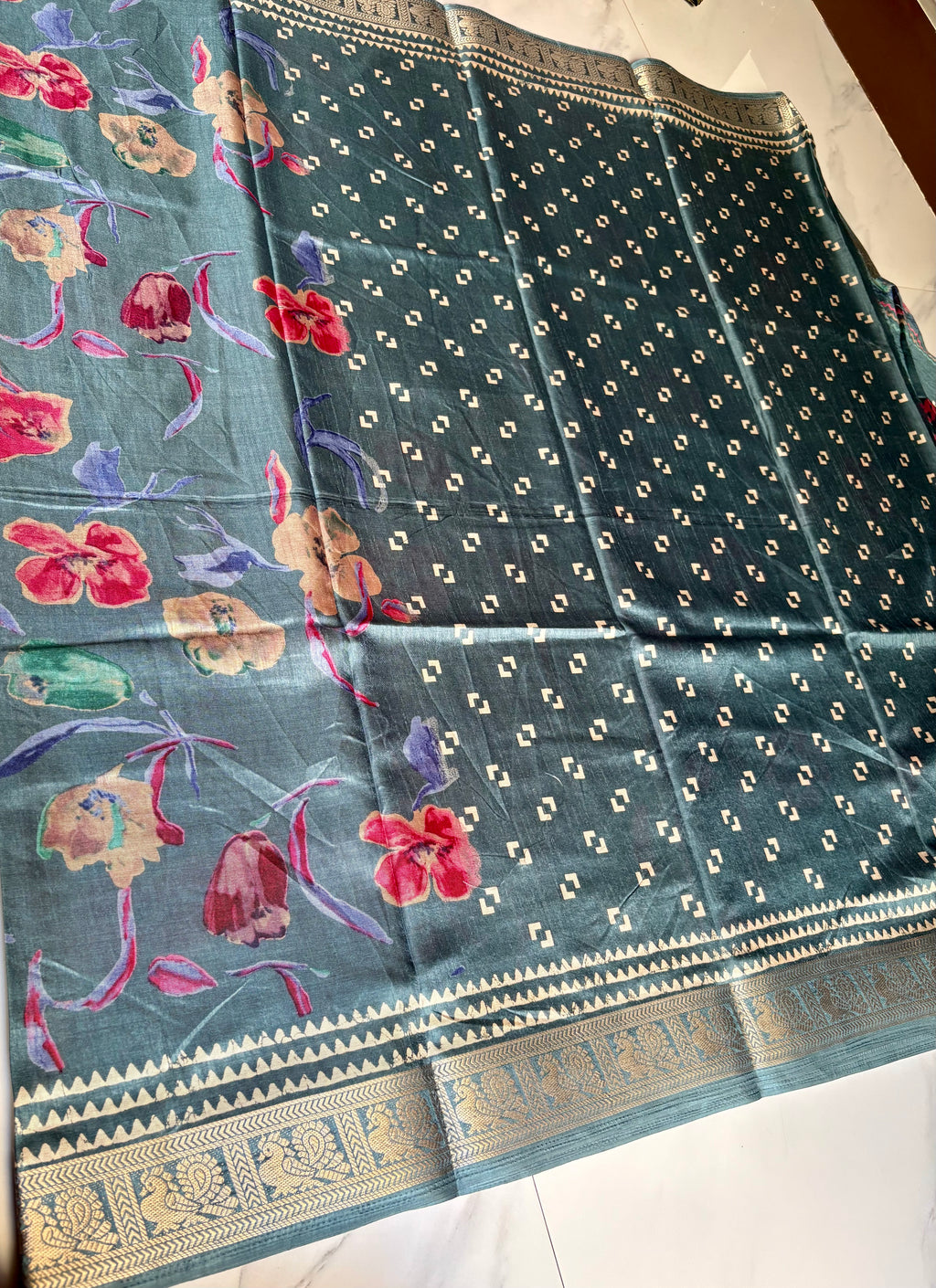 Elegant teal blue saree featuring vibrant multicolor floral prints that add a fresh and graceful charm. Finished with a rich golden woven zari border- Satin Tissue Saree