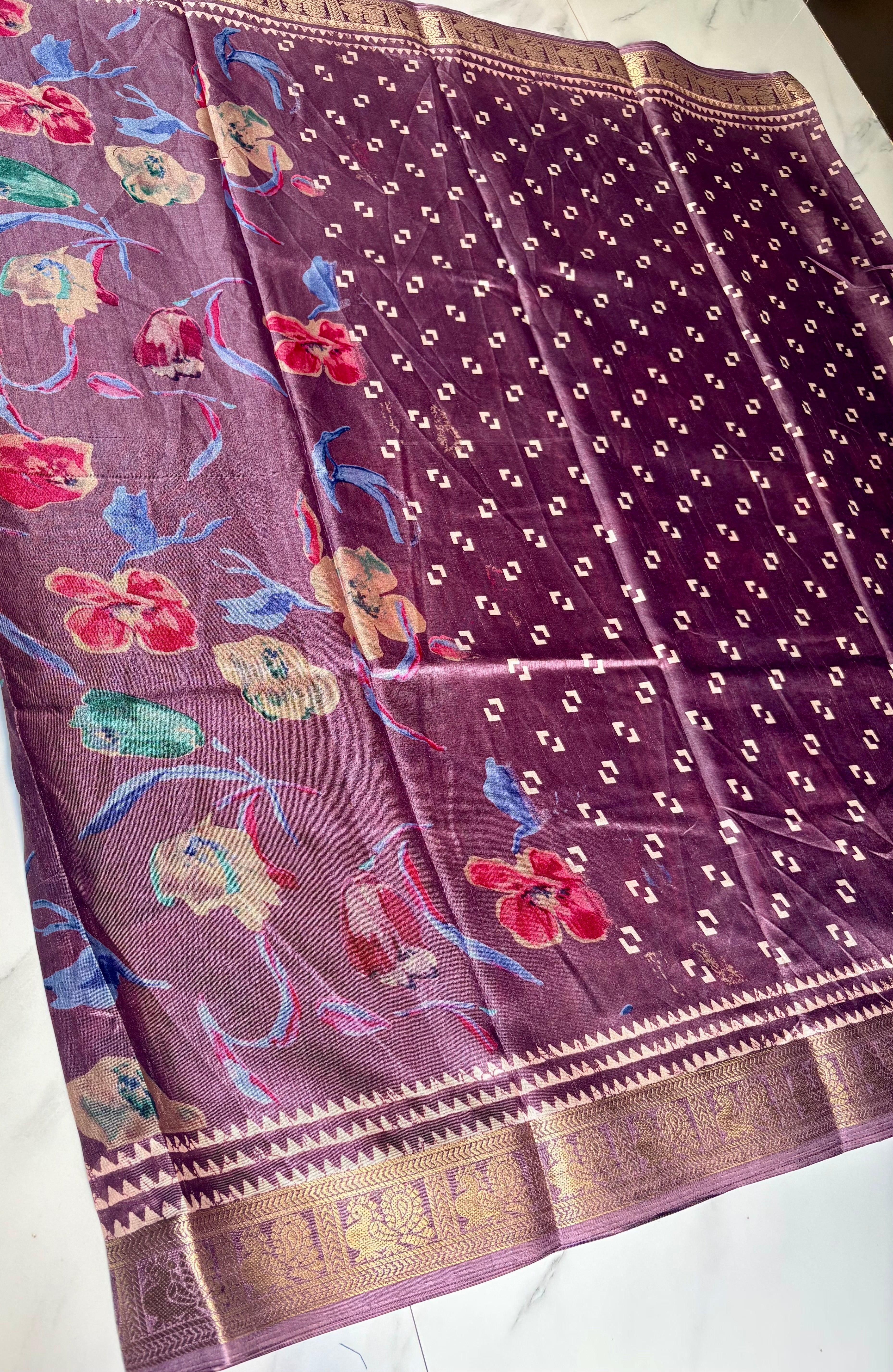 Elegant mauve-purple saree featuring a graceful floral print in vibrant shades of red, blue, and green. Accentuated with a rich golden woven border - Satin Tissue Saree