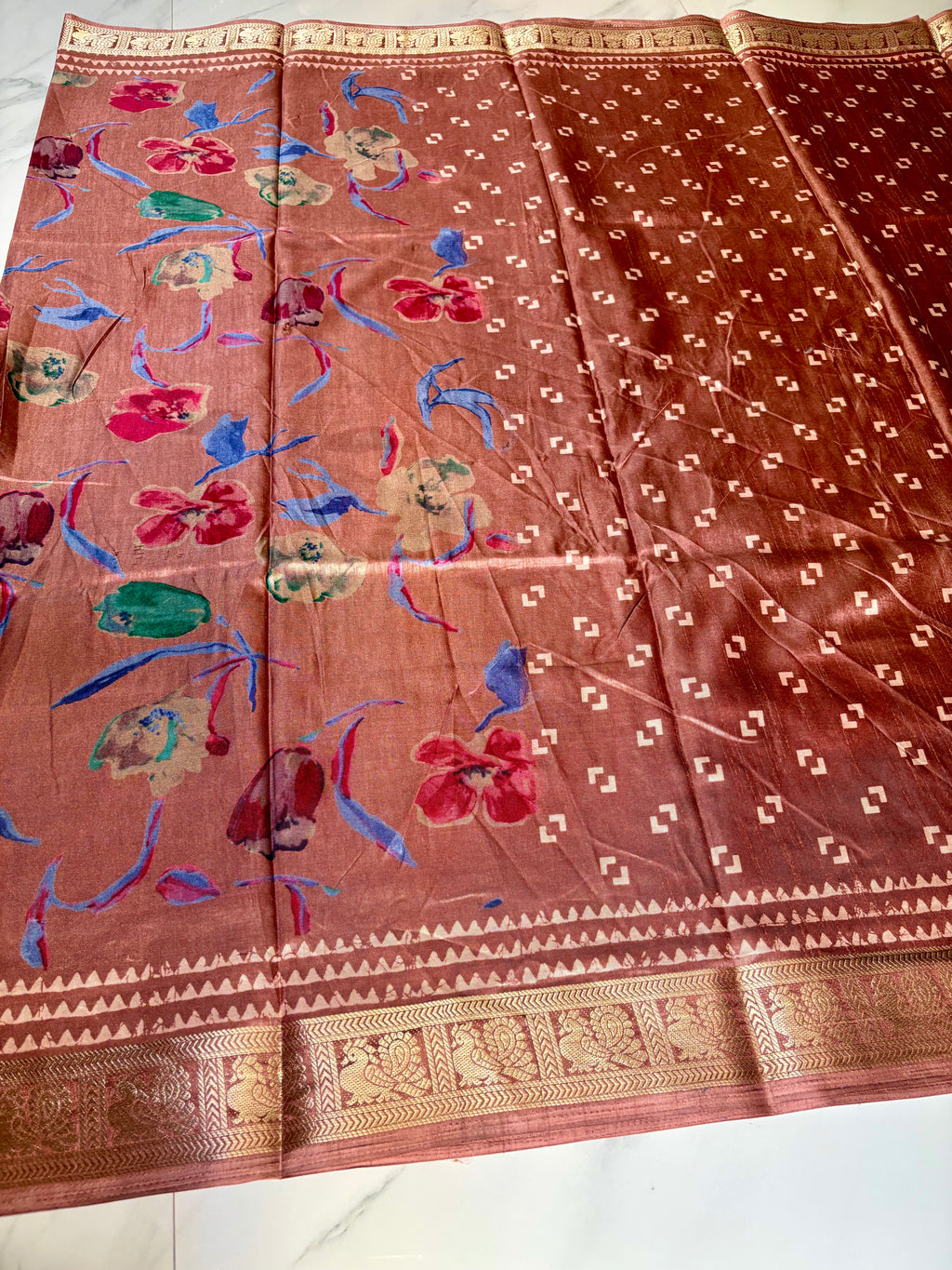 Elegant dusty rose saree featuring graceful floral prints in vibrant shades of blue, red, and beige. Finished with a rich golden woven border - Satin Tissue Saree