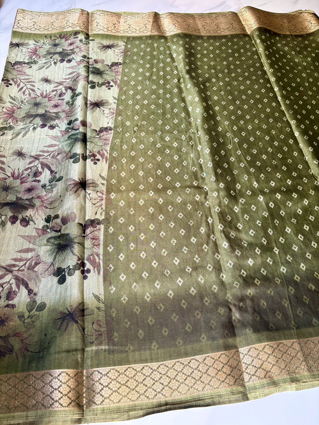 Elegant olive green saree featuring a soft floral print in earthy tones. The beautifully woven golden zari border- Satin Tissue Saree
