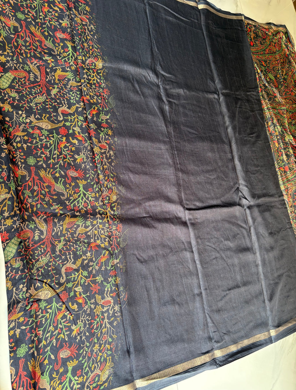 Elegant deep black saree features intricate multicolored bird, floral, and nature-inspired prints and subtle golden edging.