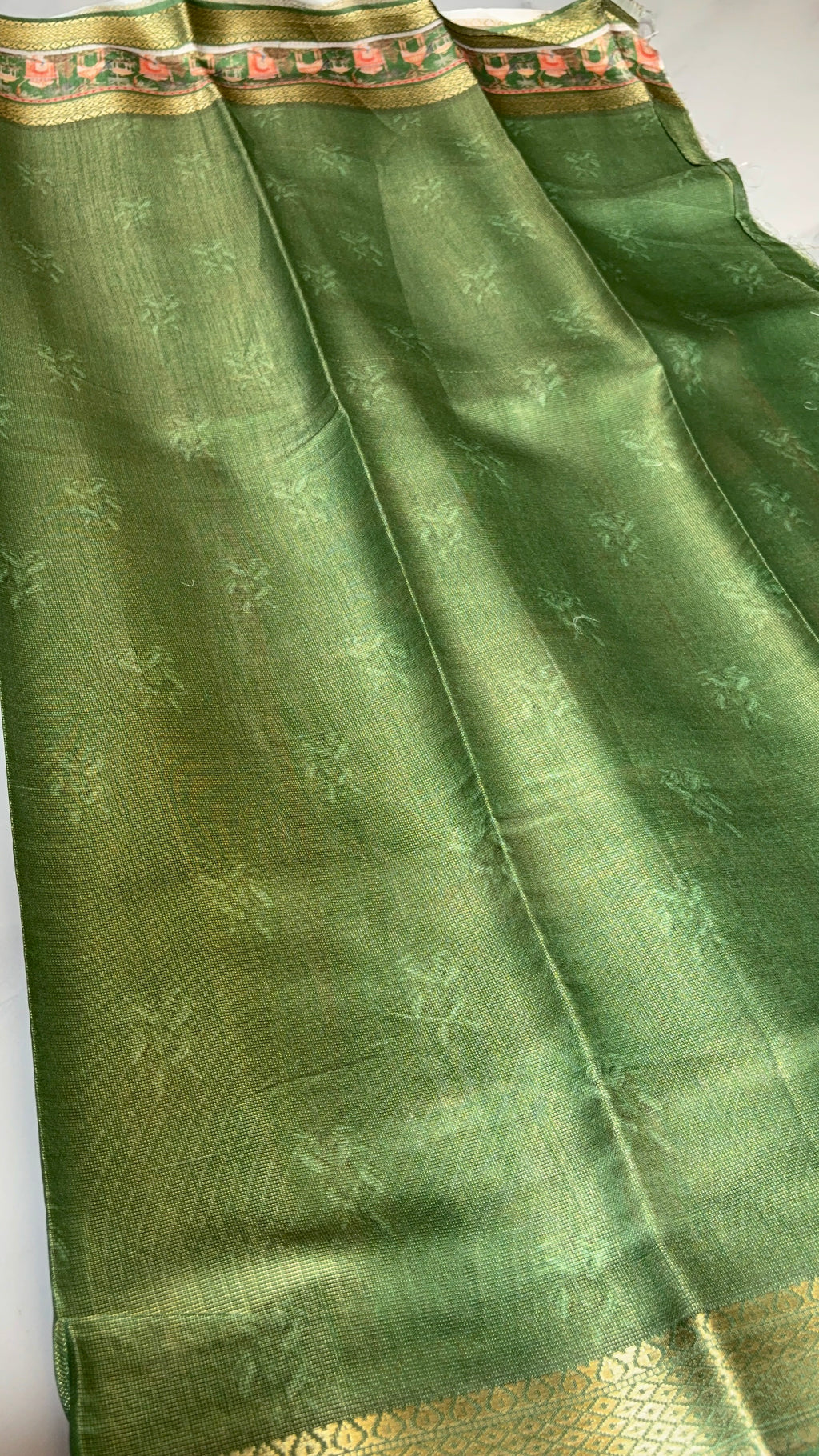 Graceful olive green saree, adorned with delicate floral motifs and heritage-inspired scenic border. Accented with intricate golden zari.