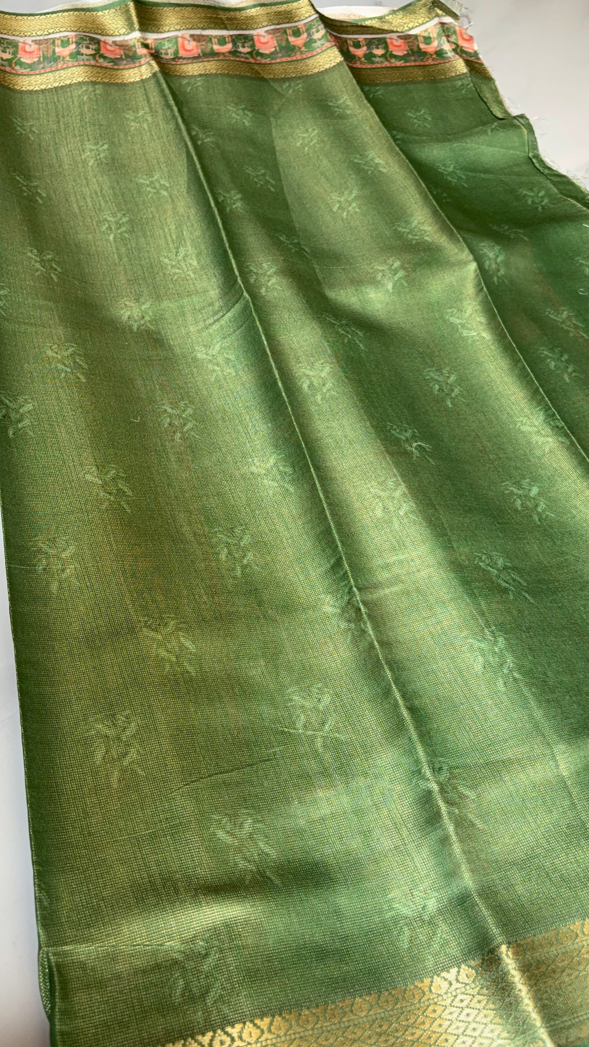 Graceful olive green saree, adorned with delicate floral motifs and heritage-inspired scenic border. Accented with intricate golden zari.