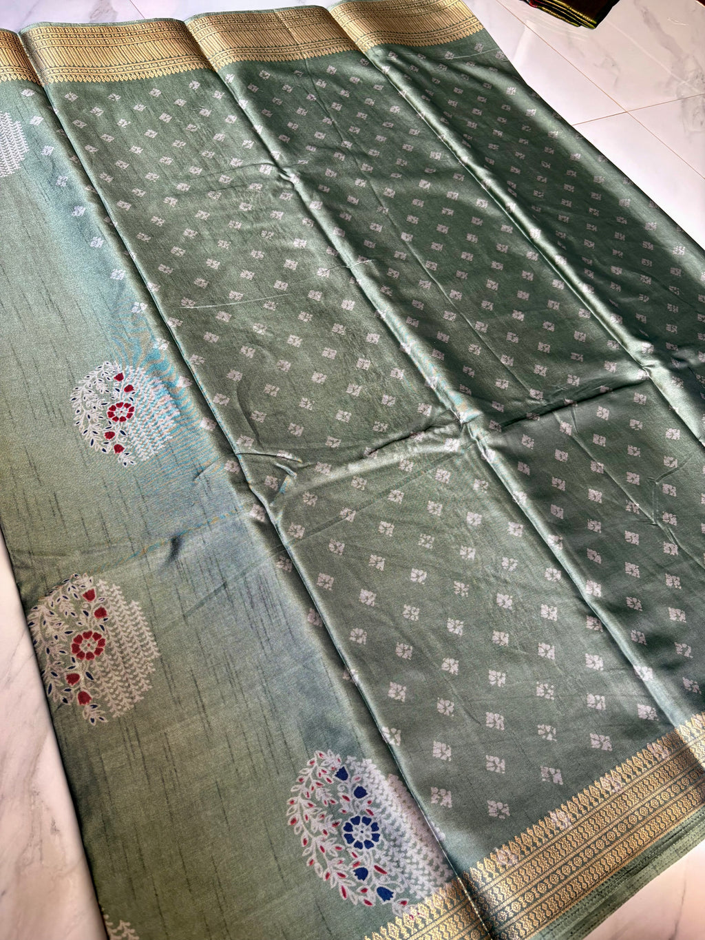 Elegant sage green silk saree, beautifully adorned with delicate floral motifs and a rich golden zari border