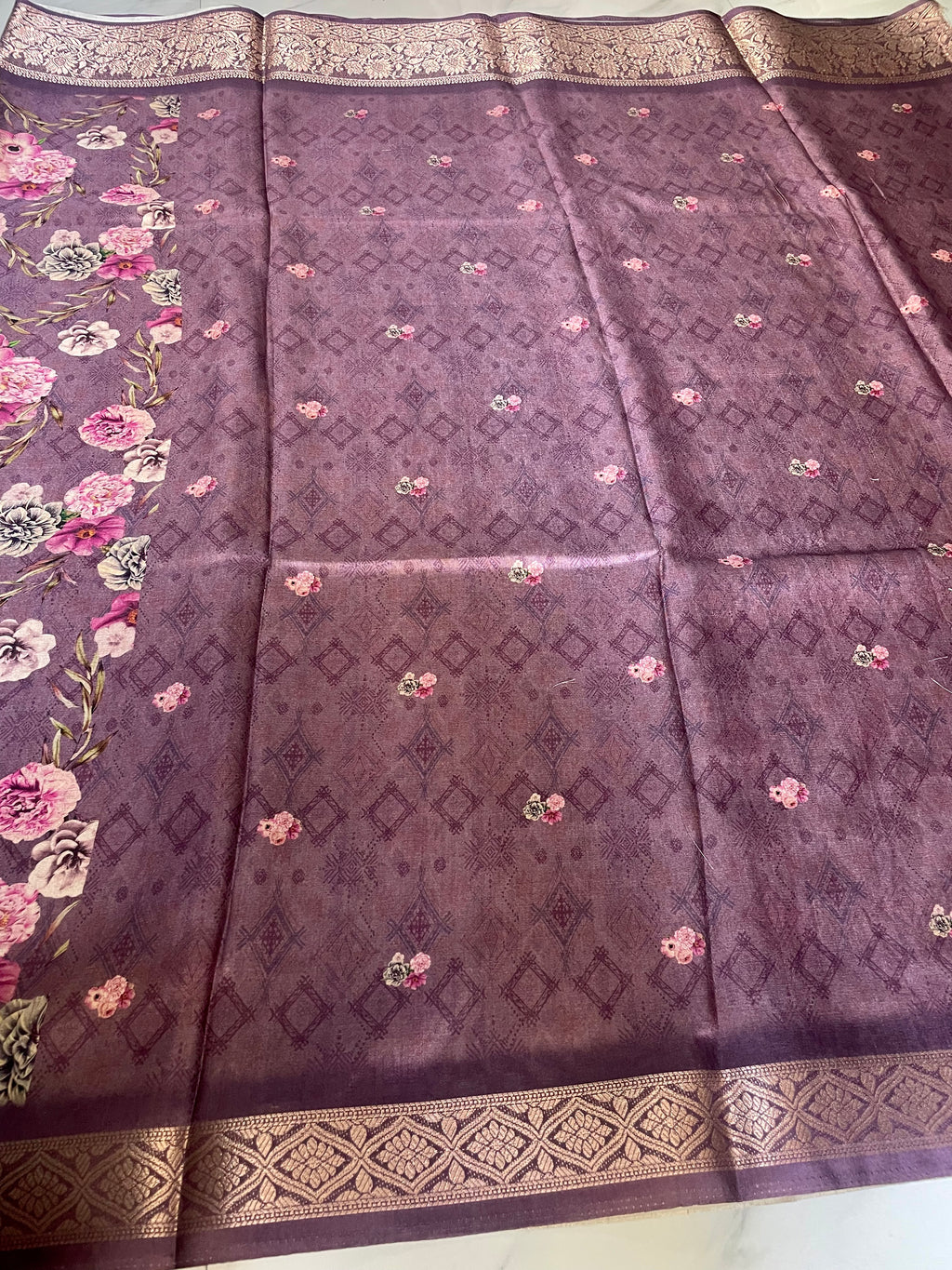 Elegant  purple floral printed saree features a beautiful all-over bloom pattern with rich woven zari border - Satin Tissue Saree